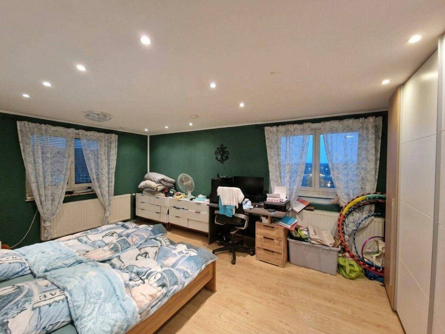 Schlafzimmer mit grün gestrichenen Wänden, Doppelbett und Einbauschränken.