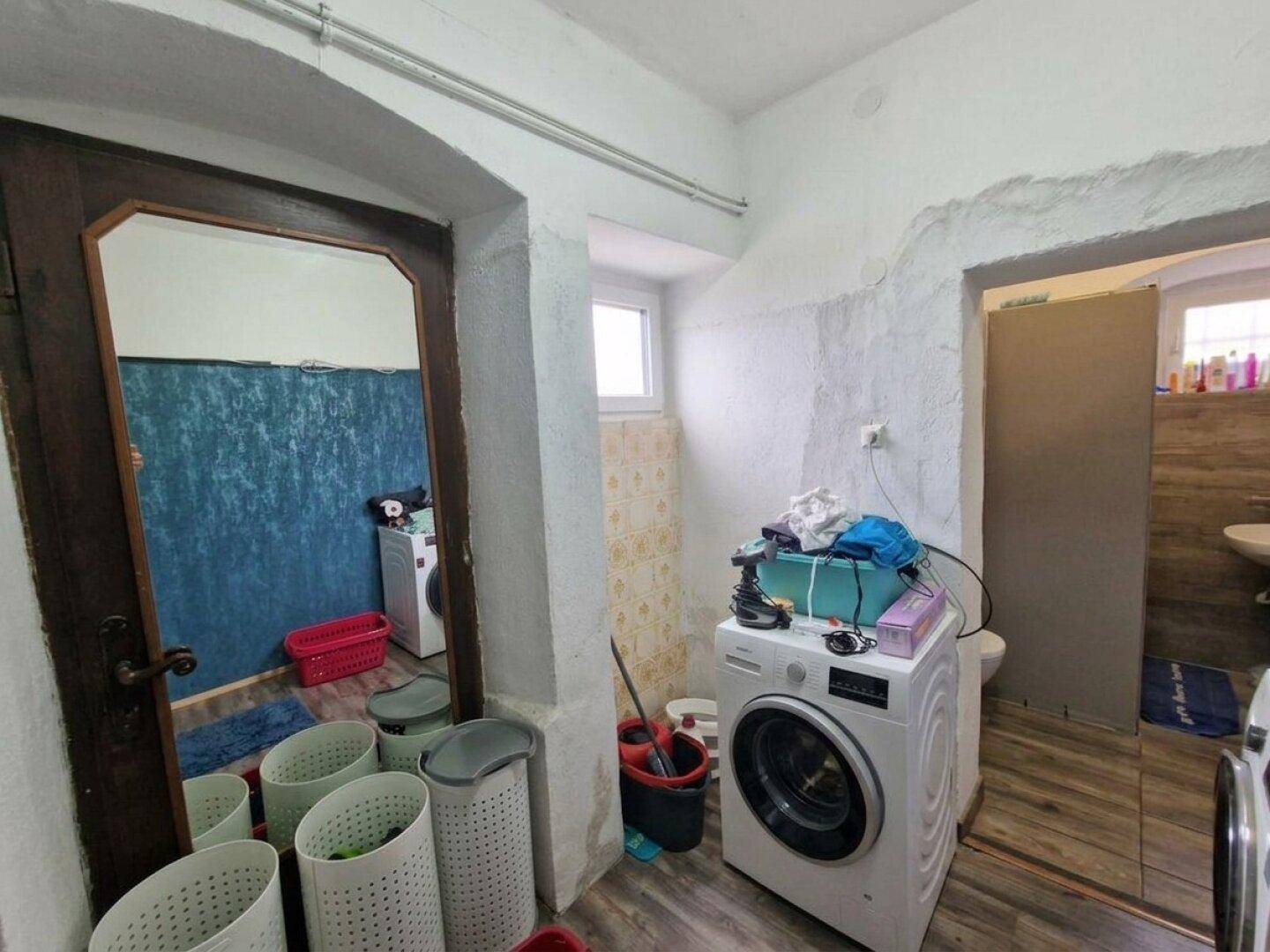 Waschküche mit Waschmaschine, Wäschekörben und Zugang zu einem weiteren Badbereich.