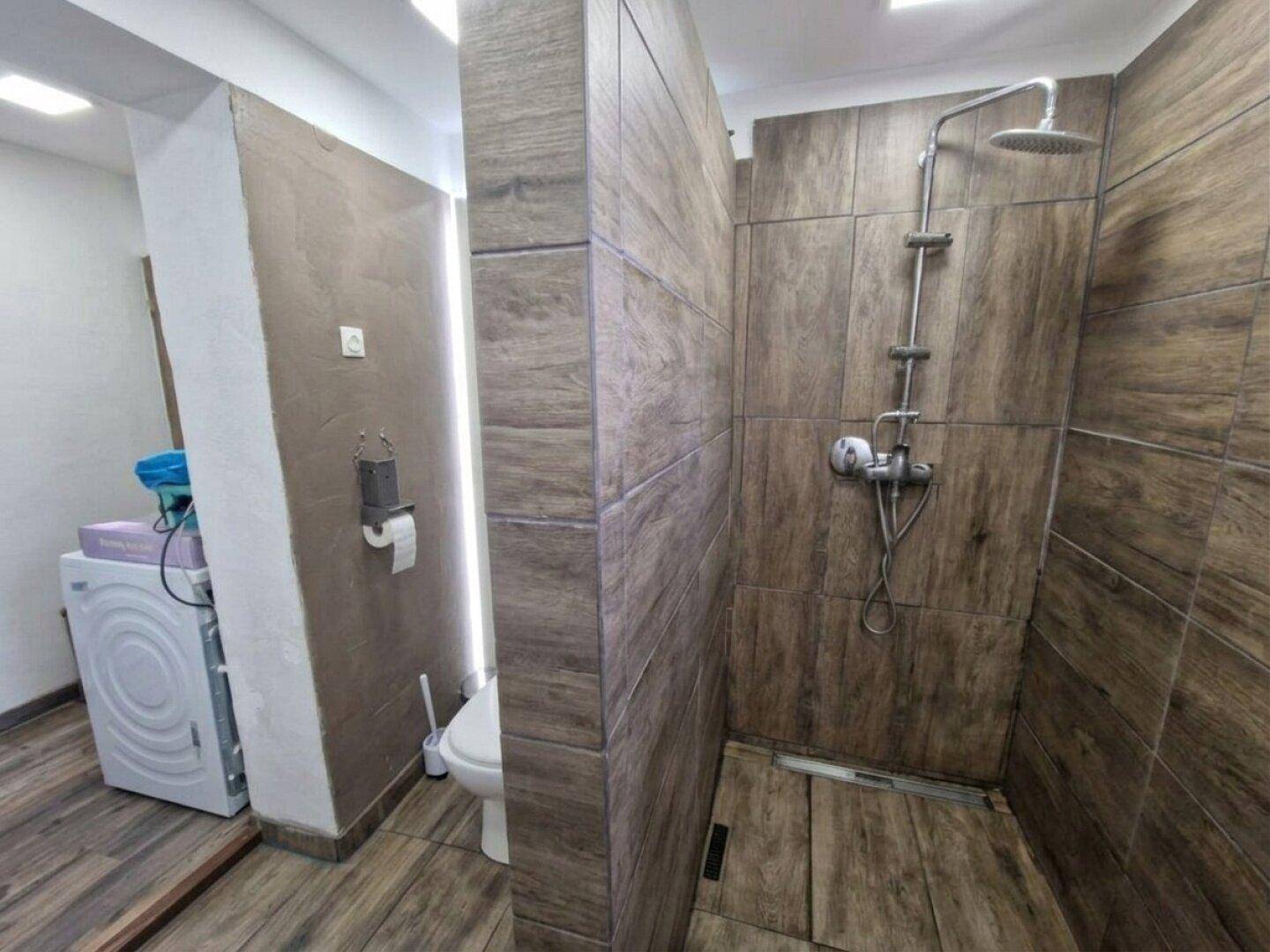 Modern geflieste Dusche mit Regenduschkopf und angrenzendem WC-Bereich.