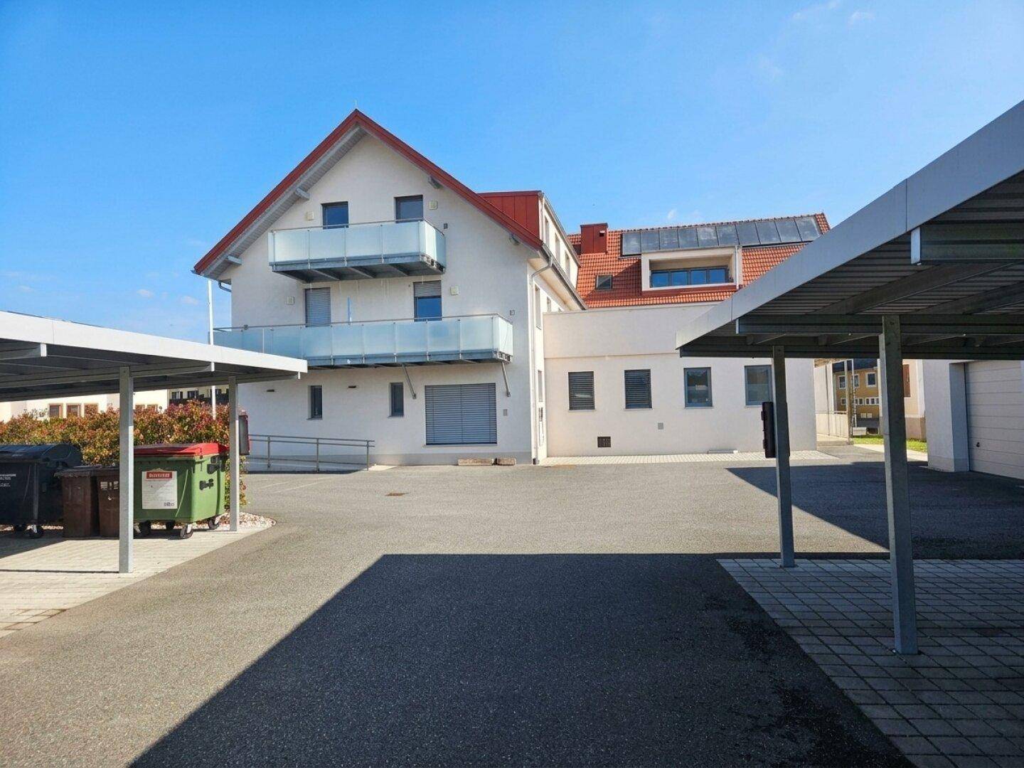 Rückansicht des Gebäudes mit Parkplätzen unter Carports und Zugang über eine Rampe.