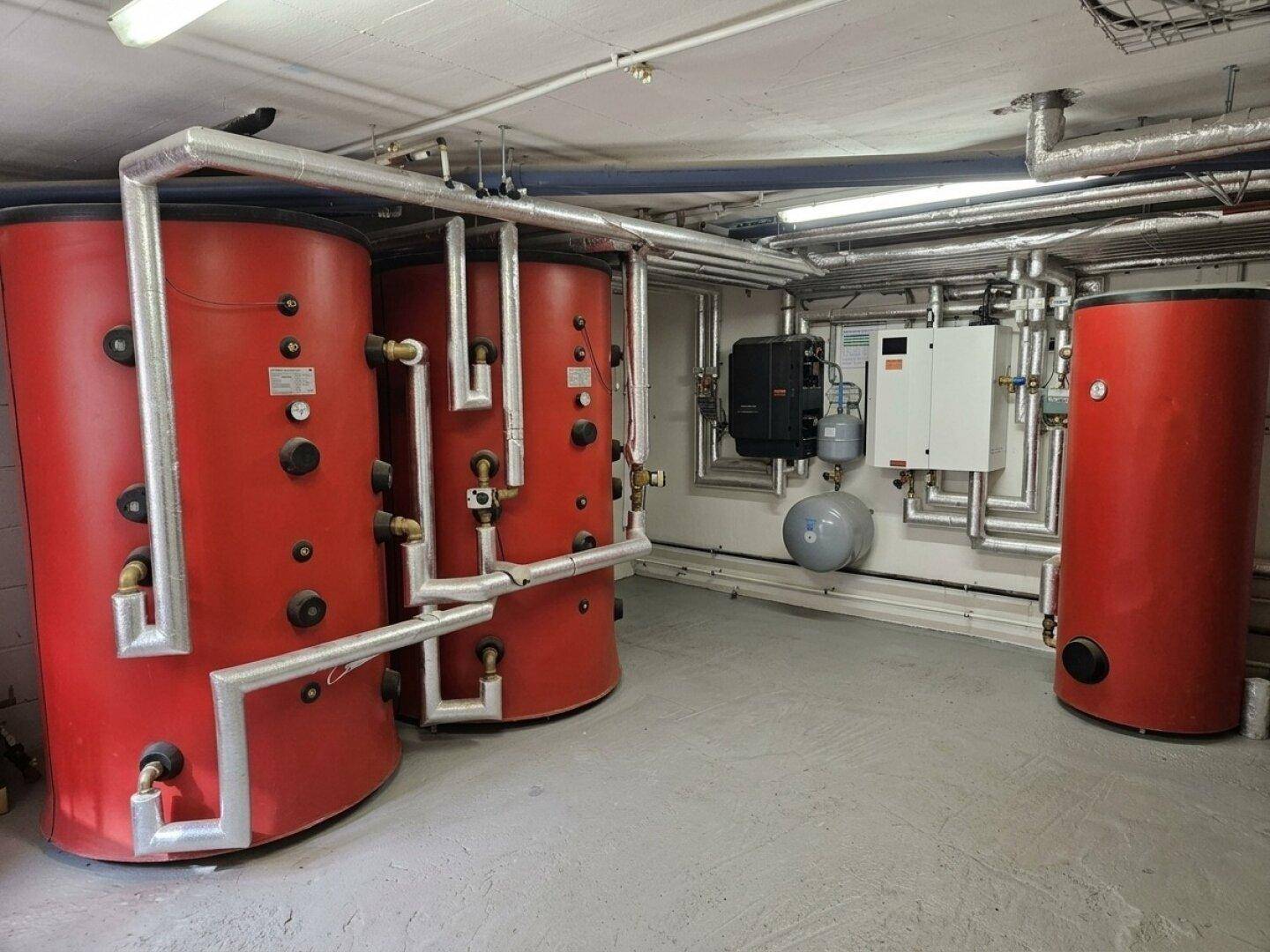 Technikraum mit mehreren großen Warmwasserspeichern und komplexen Rohrinstallationen.