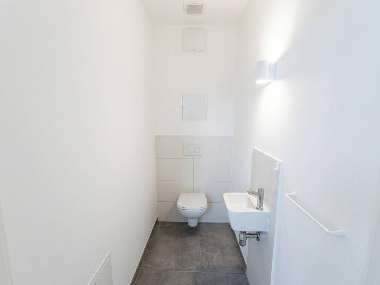 Modernes Gäste-WC mit Wand-WC, kleinem Waschbecken und dunklen Bodenfliesen.