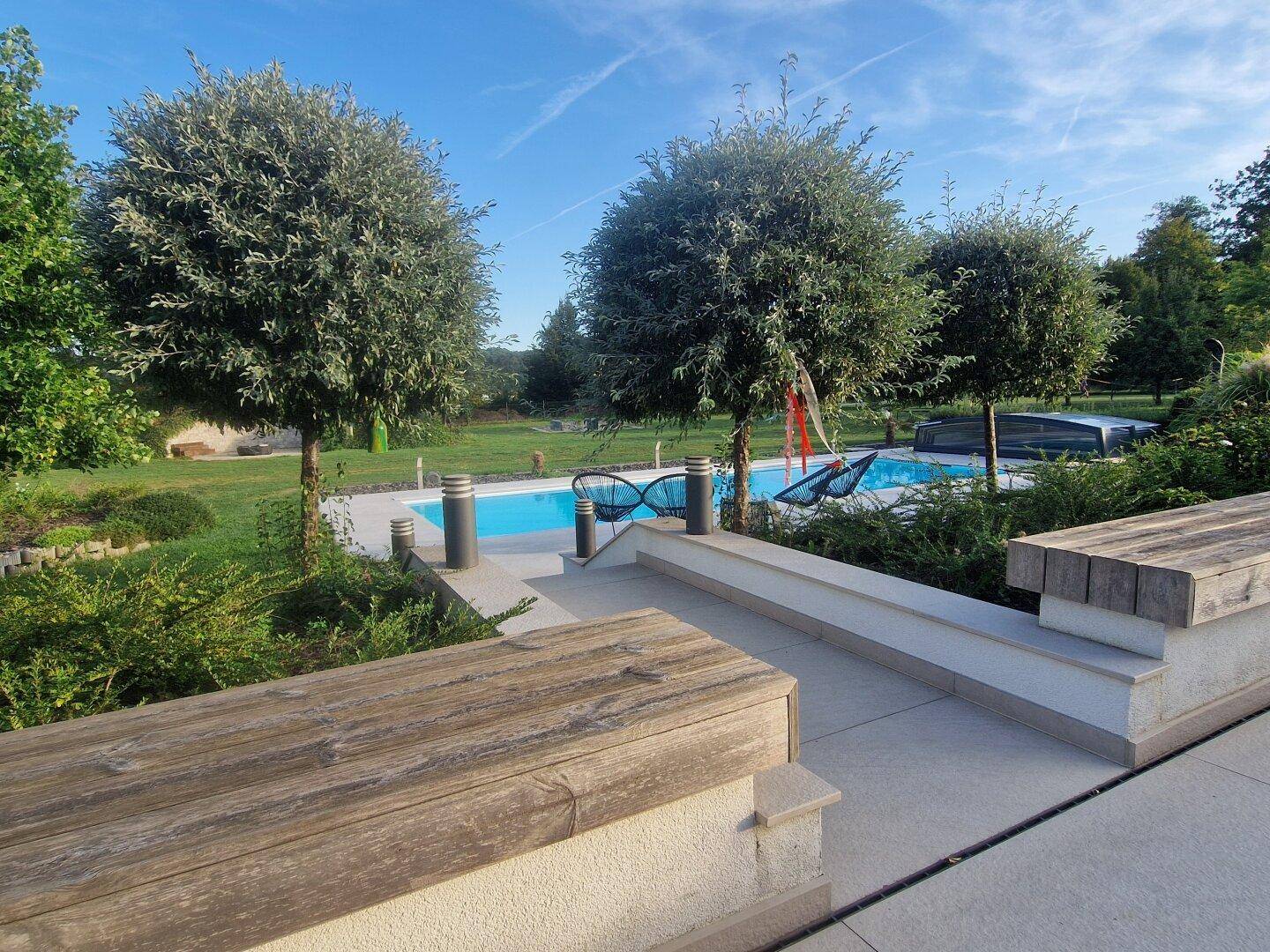 Weitläufiger Gartenbereich mit Swimmingpool, Bäumen und Holzbank für Entspannung.