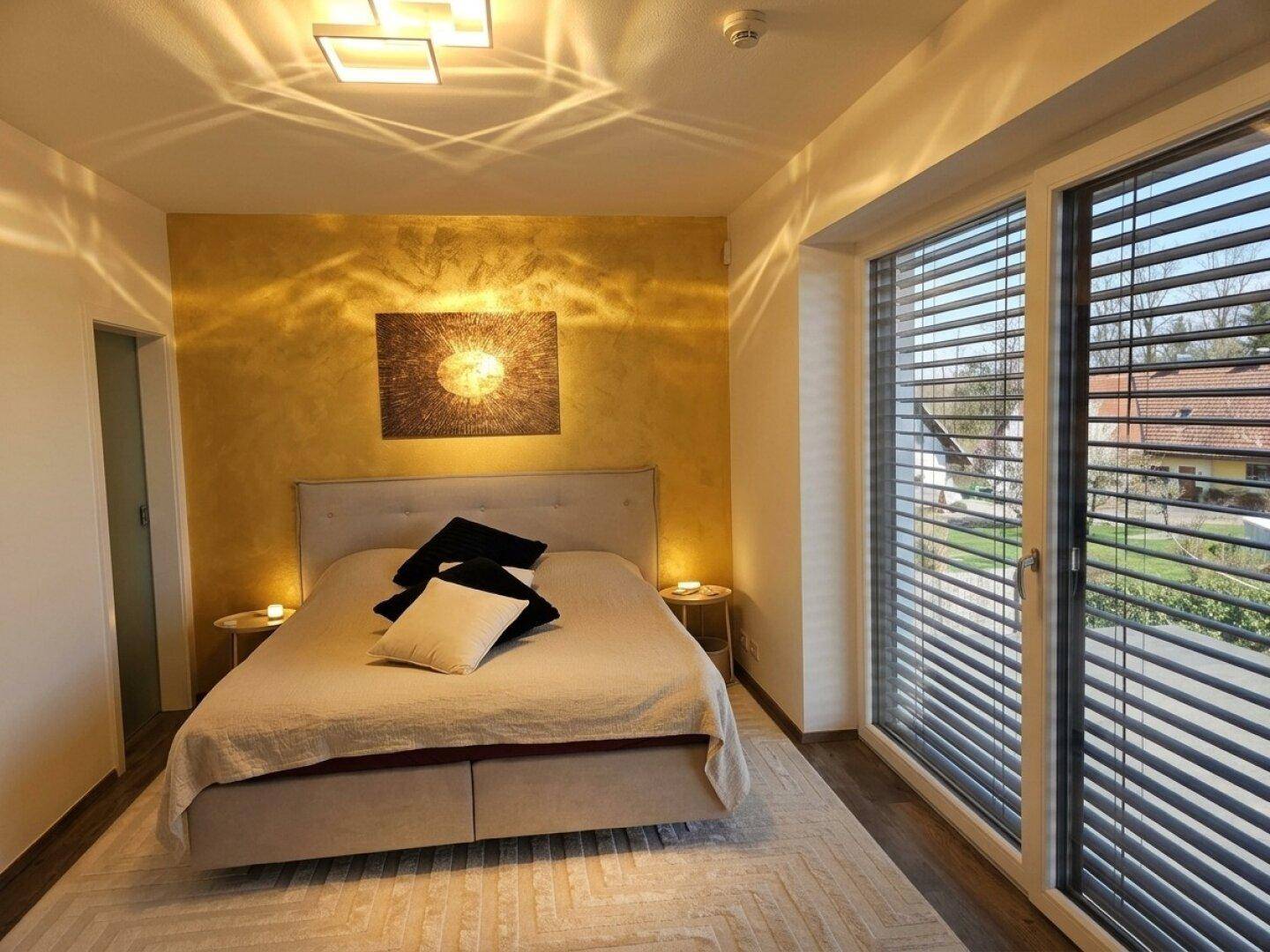 Helles Schlafzimmer mit Doppelbett, Holzboden und großer Fensterfront.