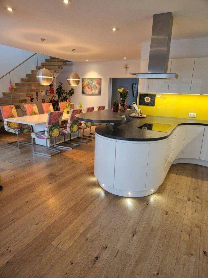 Moderne Küche mit Kochinsel und Essbereich, verbunden mit einer eleganten Holztreppe.