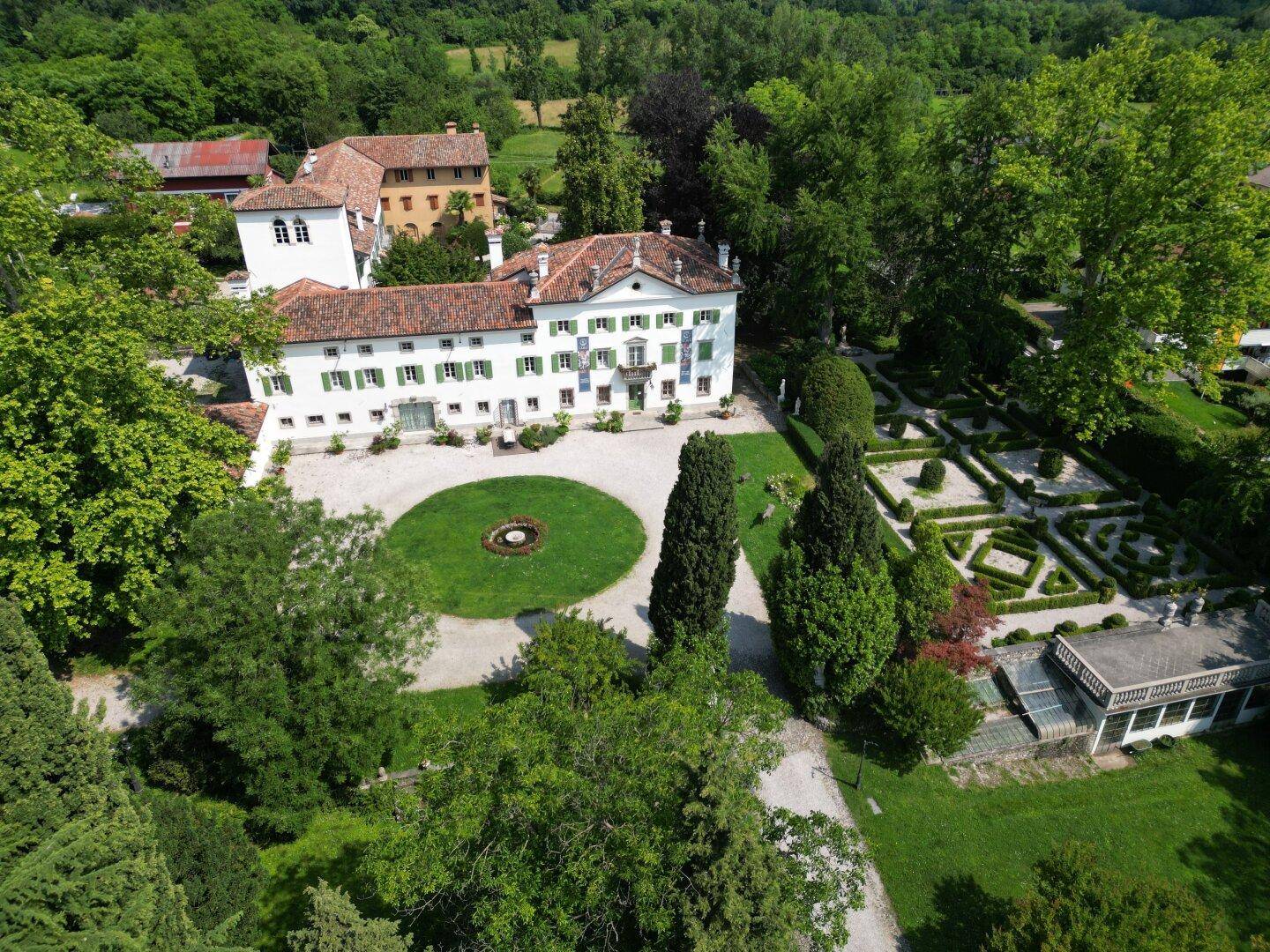 Weitläufiges Anwesen mit historischer Villa, kreisförmiger Auffahrt und gepflegtem Garten, umgeben von viel Grün.
