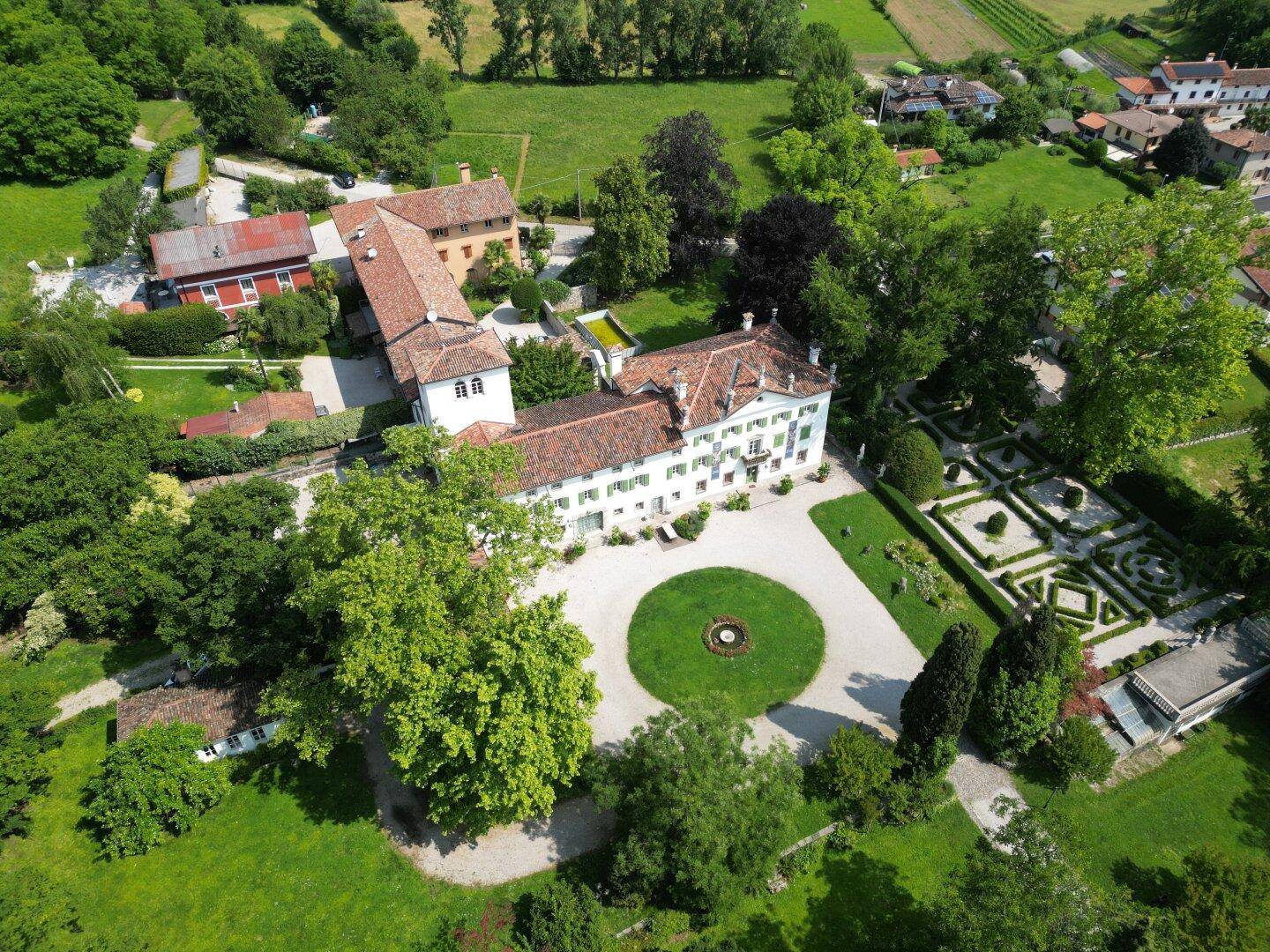 Panoramablick auf die historische Villa und ihre weitläufigen Gärten, eingebettet in eine grüne Landschaft.