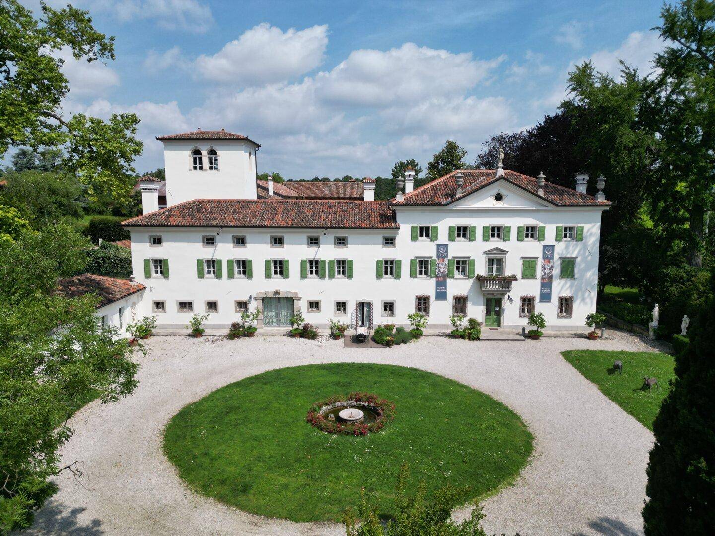 Die elegante weiße Fassade der Villa mit grünen Fensterläden und einem gepflegten Vorplatz unter blauem Himmel.