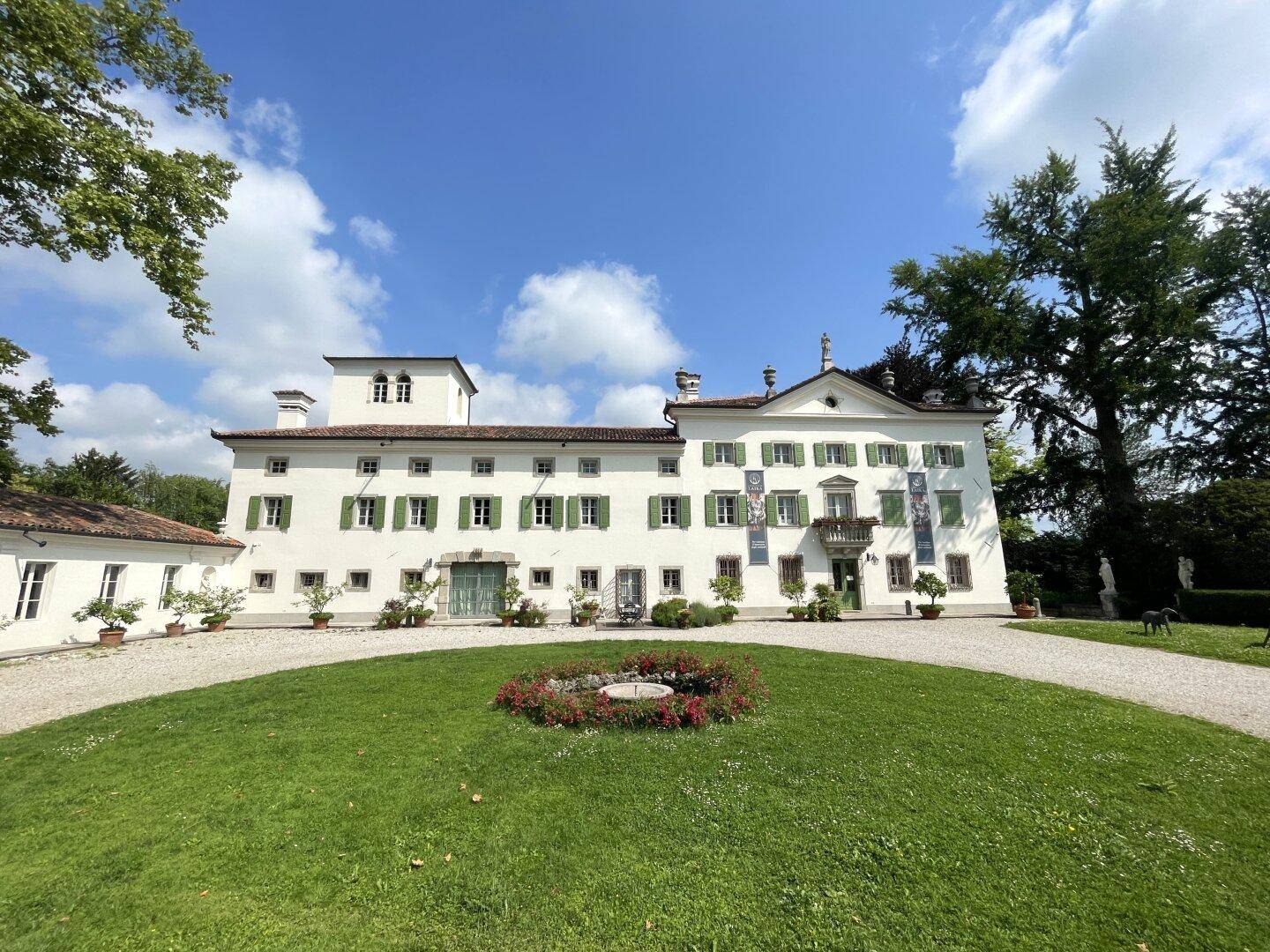 Die prächtige weiße Villa mit ihren grünen Fensterläden und einem blühenden Blumenbeet in der kreisförmigen Auffahrt.