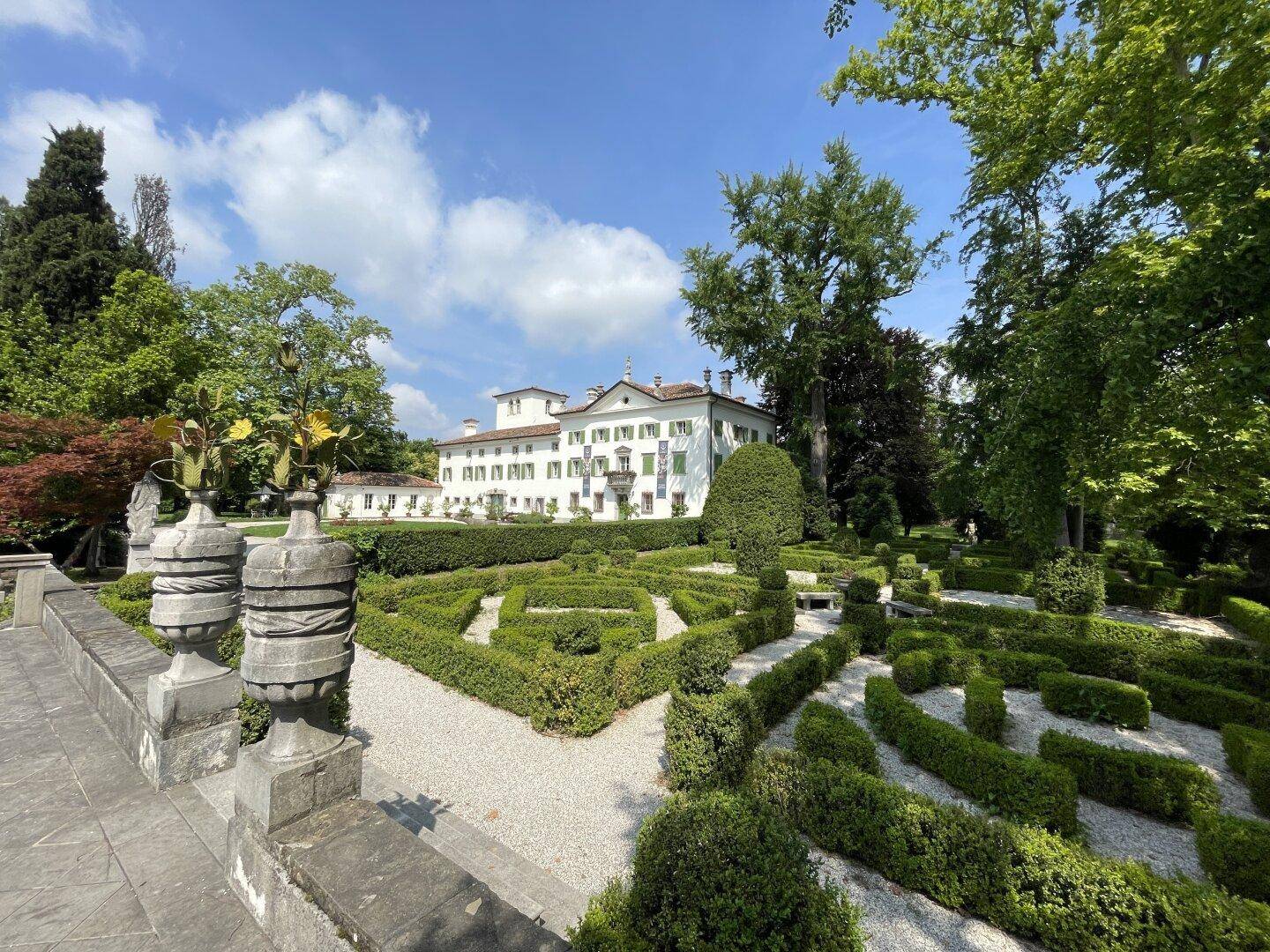 Der kunstvoll gestaltete formale Garten mit geschnittenen Hecken, Kieswegen und klassischen Statuen im Sonnenlicht.