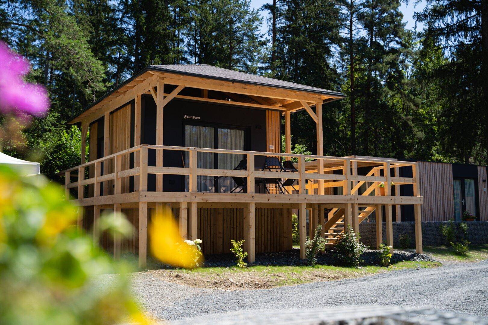 Idyllisches Ferienhaus mit großer Holzterrasse, umgeben von üppiger Vegetation und Bäumen.