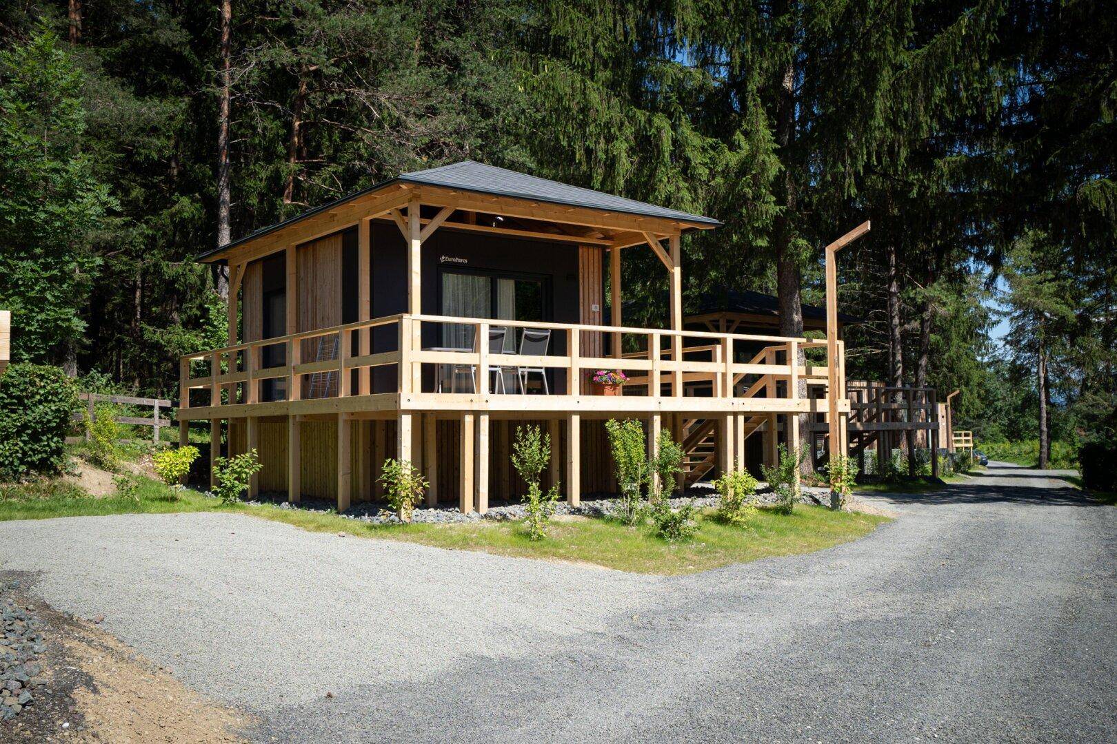 Kleines Ferienhaus mit erhöhter Holzterrasse und Zugang über eine Außentreppe, umgeben von Natur.