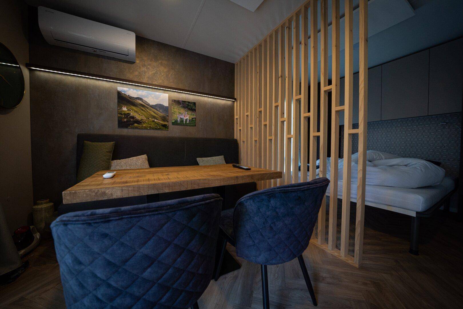 Gemütlicher Wohn- und Essbereich mit Holztisch, bequemen Stühlen und integriertem Schlafbereich.