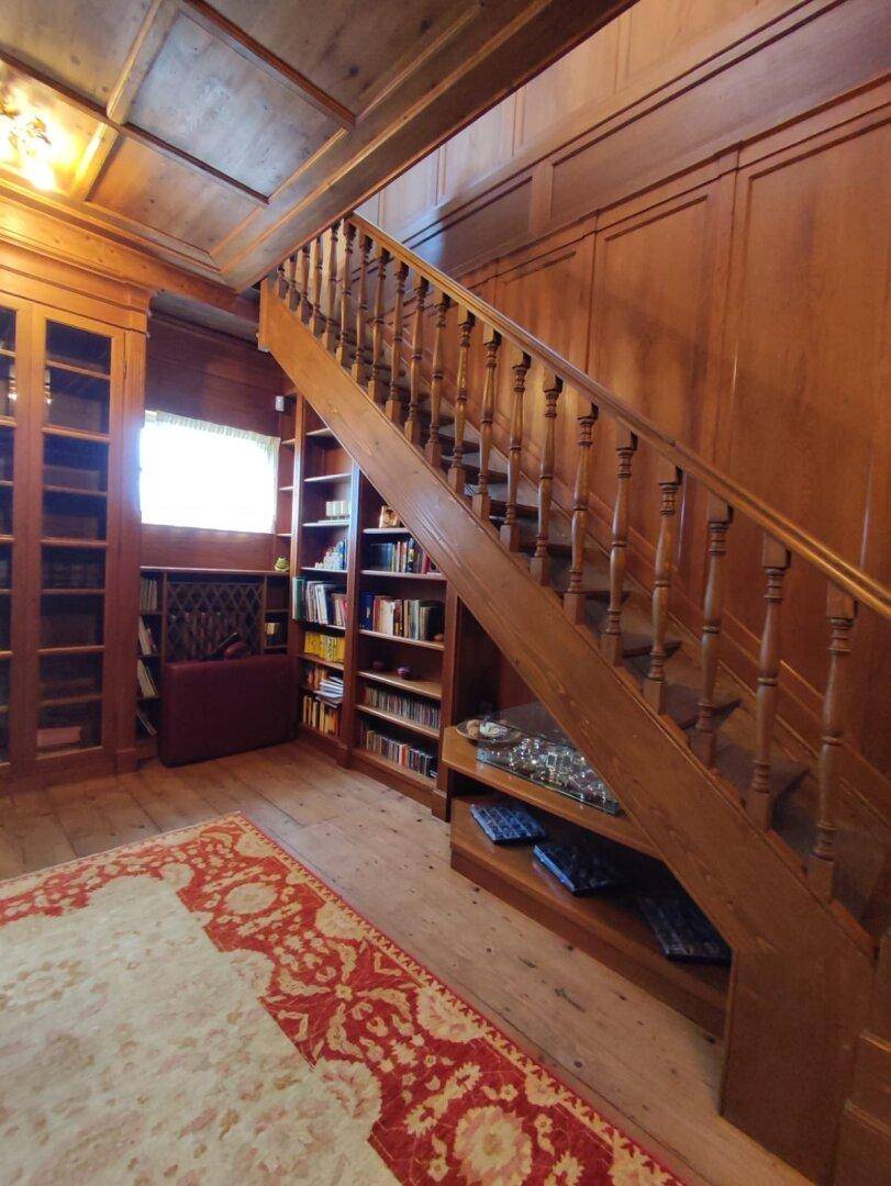 Holzvertäfelte Bibliothek mit eingebauten Bücherregalen und einer Holztreppe, die zum Lesen einlädt.