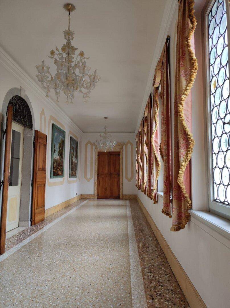 Lange Galerie mit Terrazzoboden, hohen Fenstern und eleganten Vorhängen, beleuchtet von Kronleuchtern.
