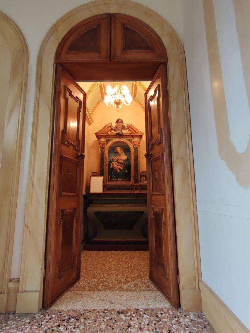 Eine kleine Nische oder Kapelle mit religiösem Gemälde und kunstvollen Holztüren, die eine intime Atmosphäre schafft.