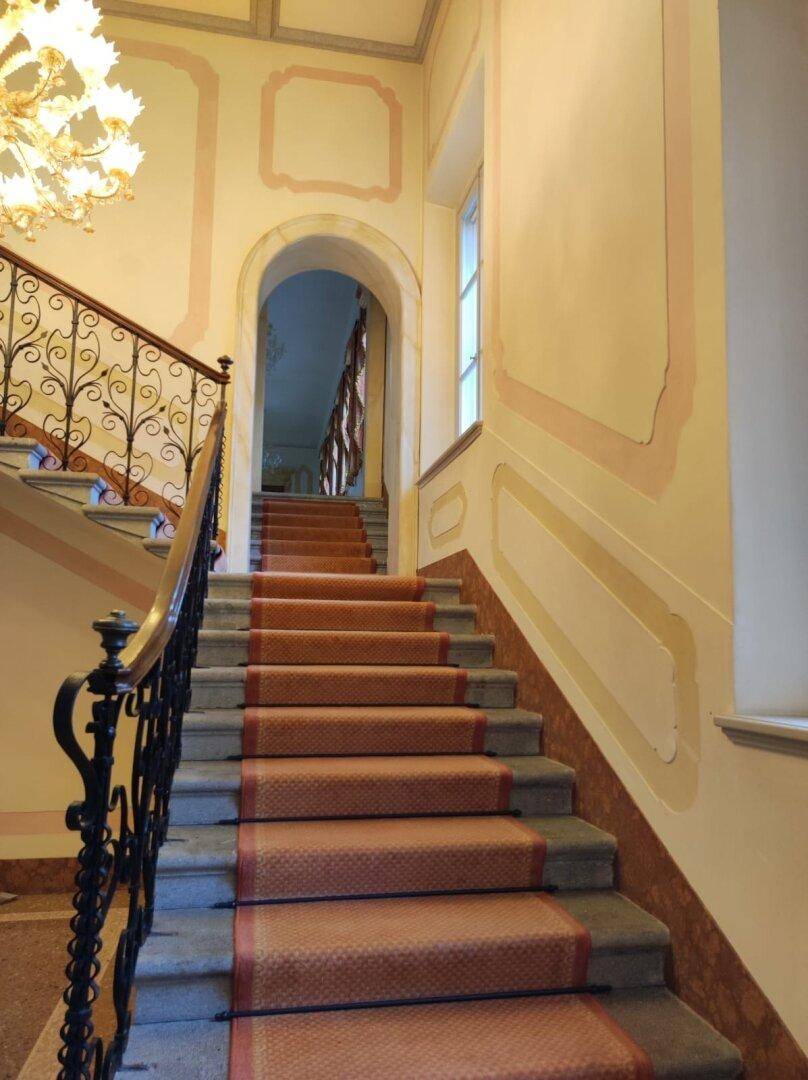 Die breite Steintreppe mit rotem Teppichläufer und kunstvollem schmiedeeisernem Geländer führt in die oberen Stockwerke.