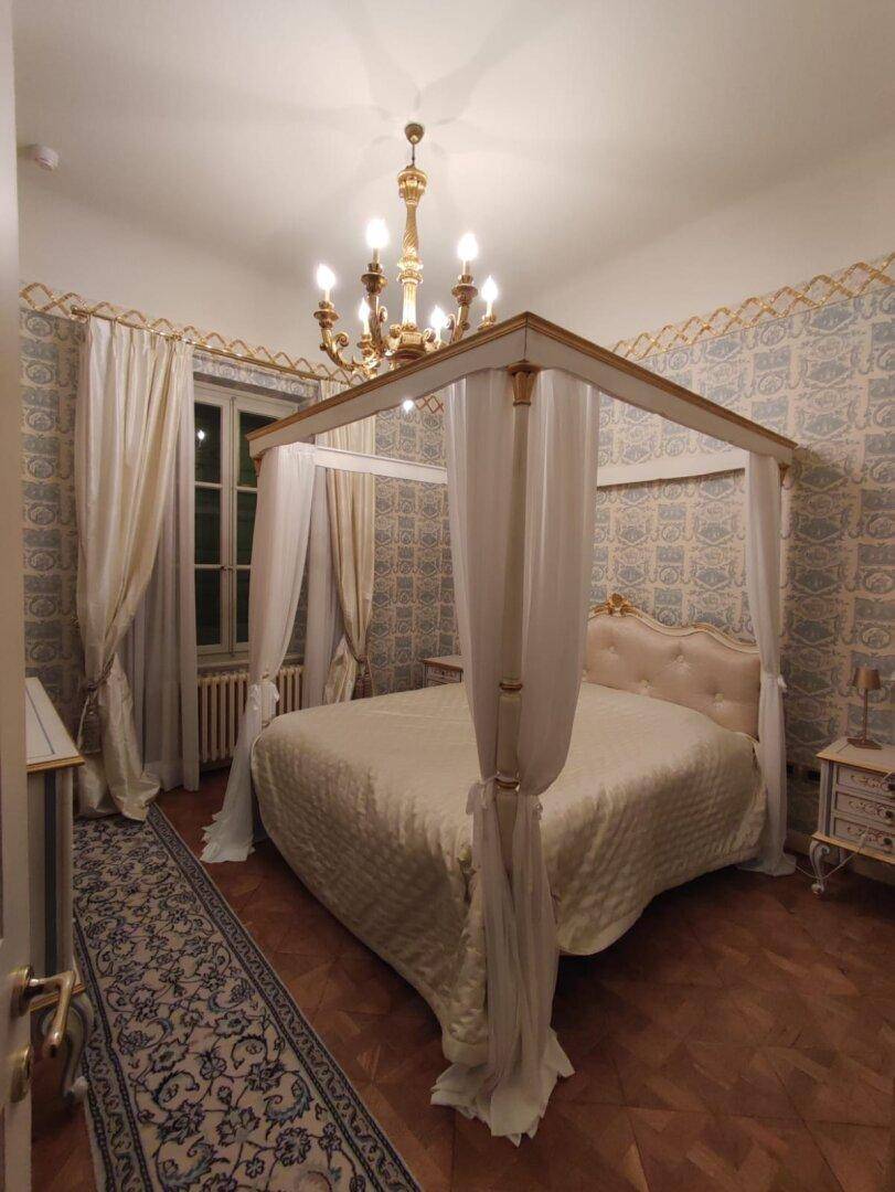 Elegantes Schlafzimmer mit Himmelbett, Parkettboden und klassischer Tapete, die eine ruhige Atmosphäre schafft.