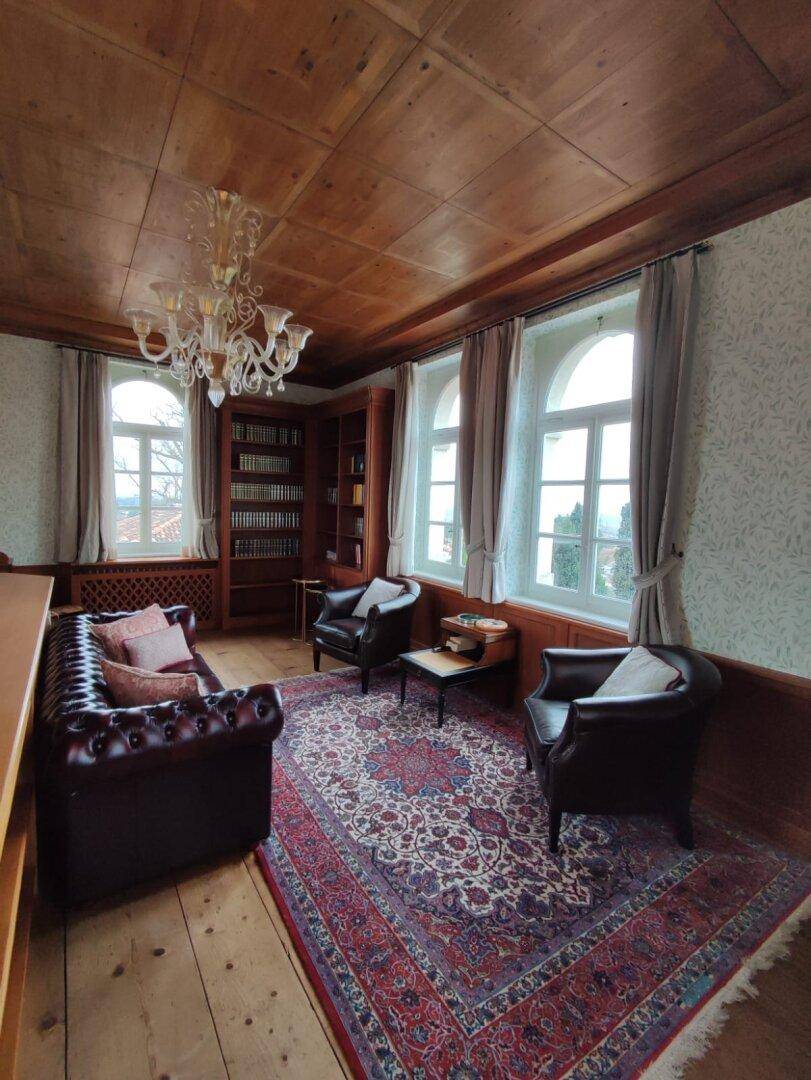 Gemütliche Bibliothek mit Holzboden, Ledersofas und Blick ins Grüne, ideal für entspannte Lesestunden.