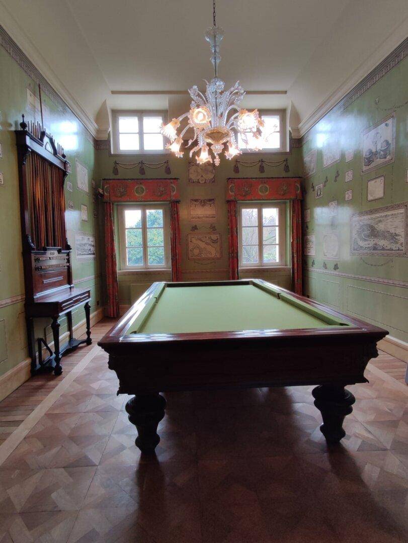 Der Billardraum mit elegantem Billardtisch, Parkettboden und dekorativer Tapete, perfekt für Unterhaltung.