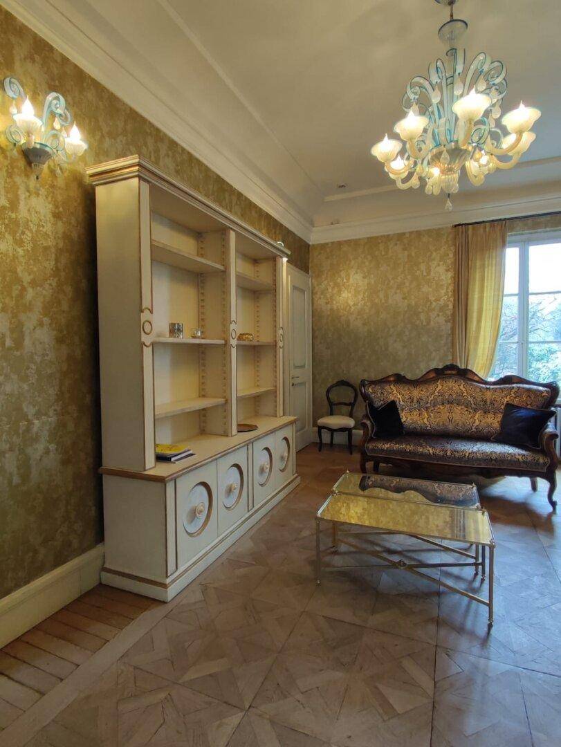 Elegantes Wohnzimmer mit Parkettboden, großem Bücherregal und goldener Tapete, die eine luxuriöse Atmosphäre schafft.