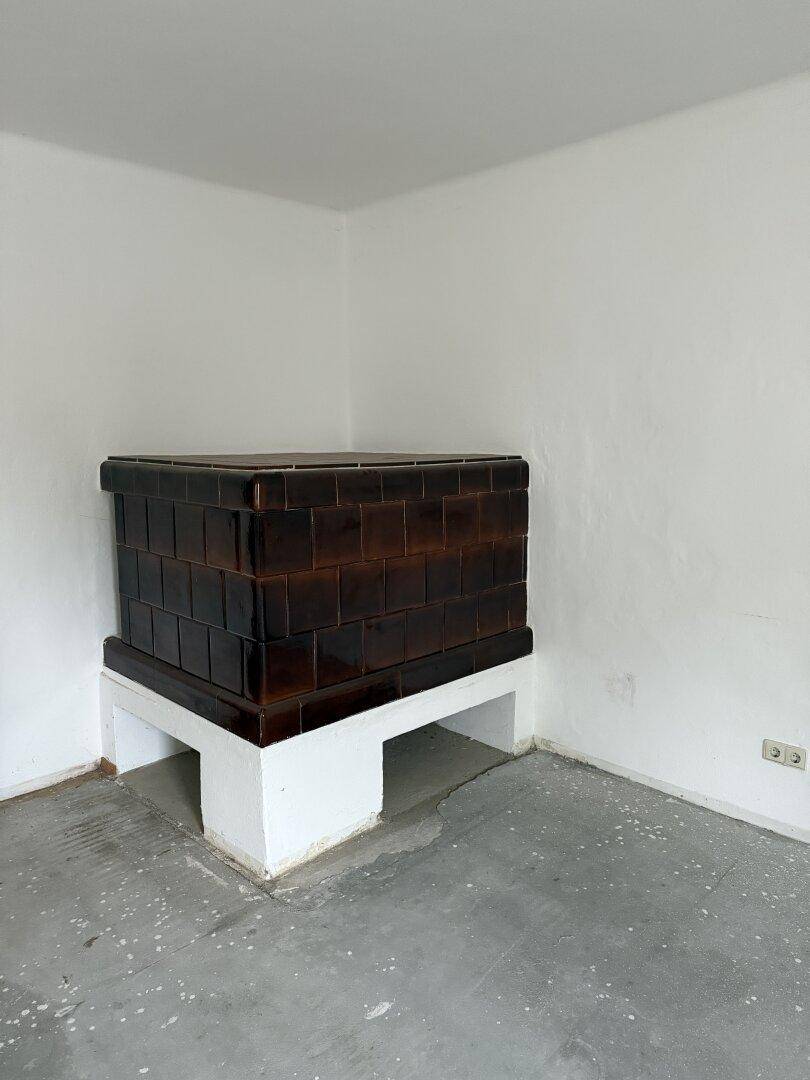 Detailansicht eines traditionellen braunen Kachelofens in einem leeren Raum mit Betonboden.