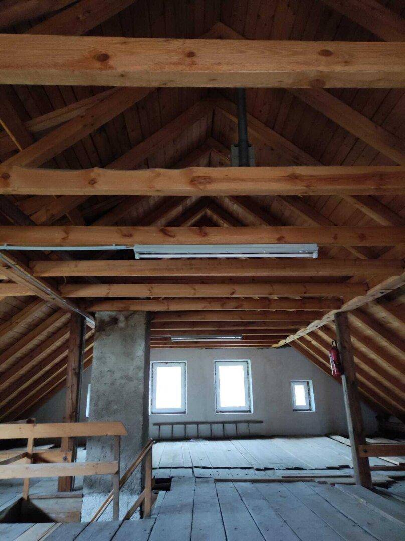 Geräumiger Dachboden mit sichtbaren Holzbalken und Fenstern, bereit für den Ausbau.