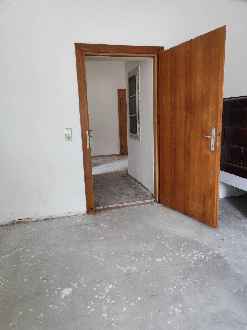 Leerer Raum mit Holztürrahmen und Betonboden, bereit für Renovierung und individuelle Gestaltung.