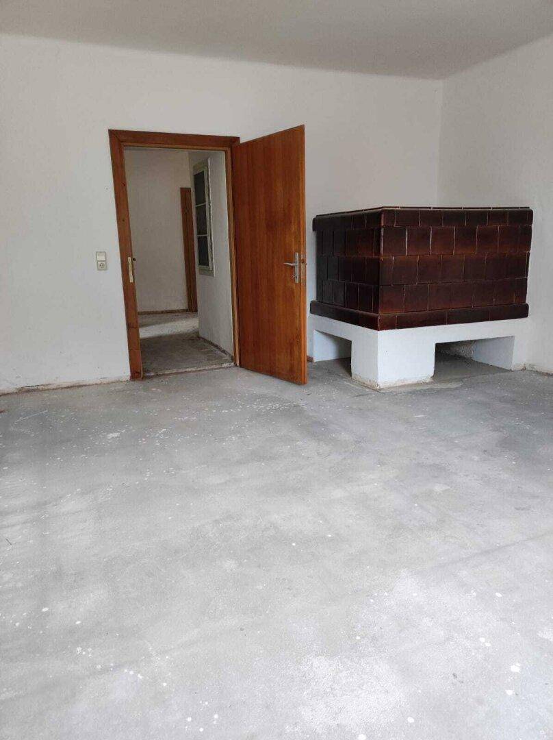 Geräumiger Raum mit traditionellem Kachelofen und Betonboden, ideal für gemütliche Stunden.