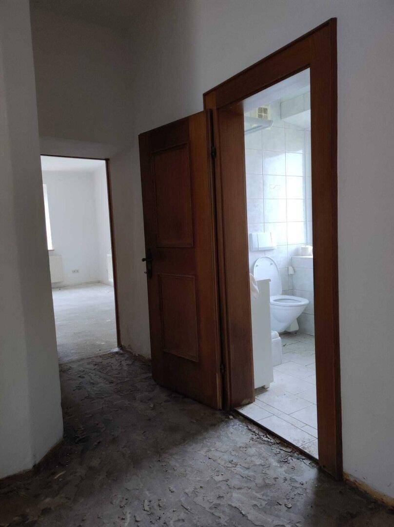 Flur mit offener Holztür, die einen Blick in ein gefliestes Badezimmer mit Toilette freigibt.