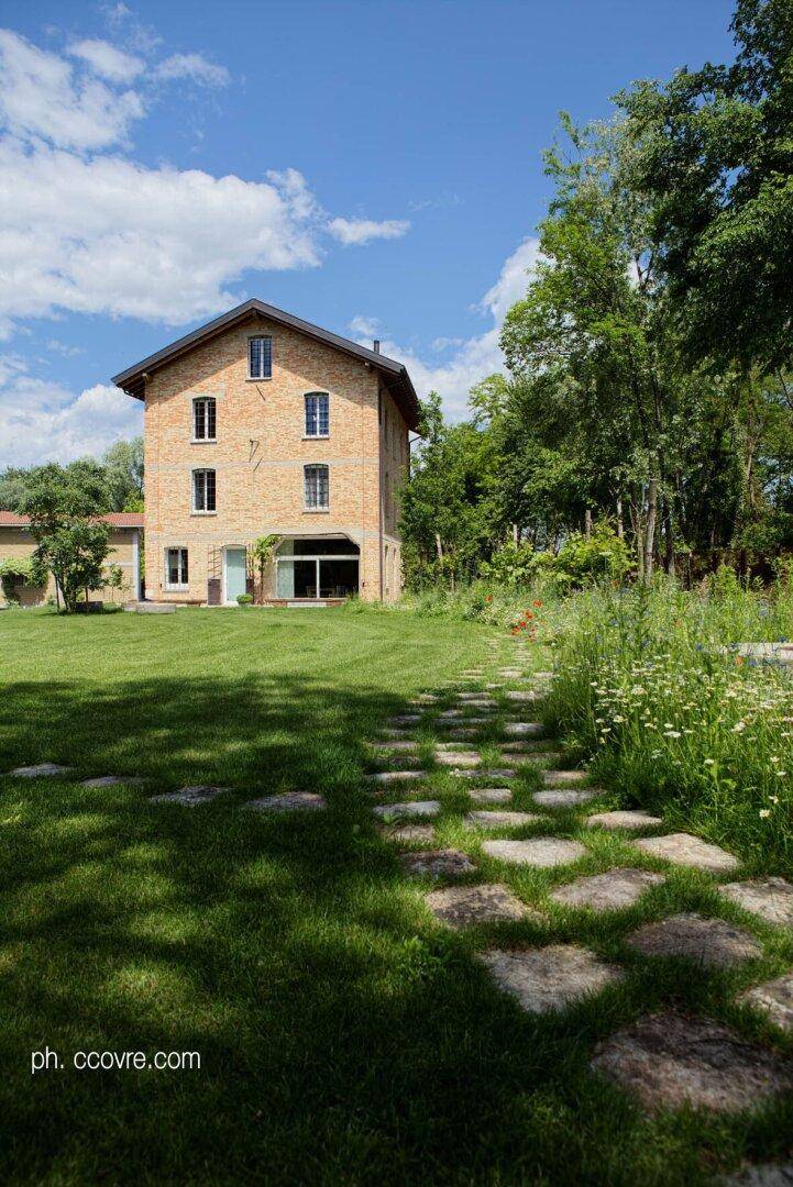 Seitlicher Blick auf das Ziegelsteinhaus mit Rasenfläche, Trittsteinen und wilden Blumen am Rand.