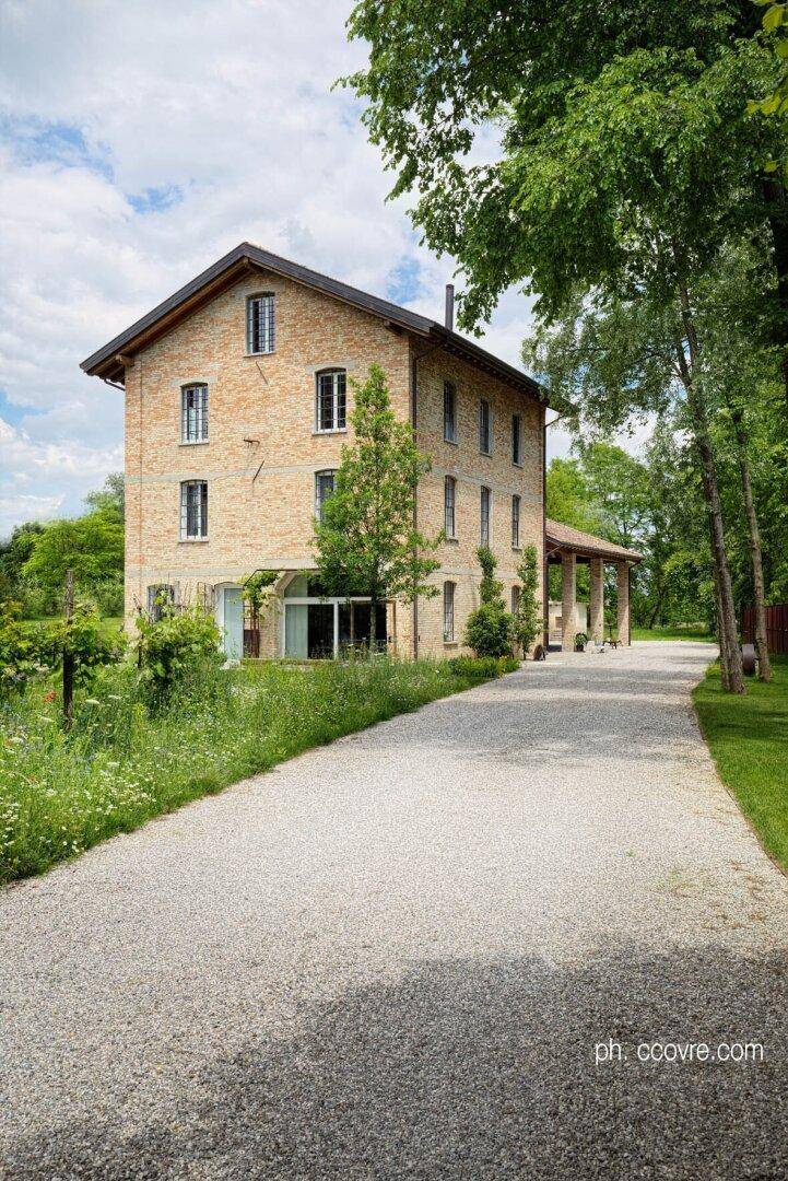 Das Ziegelsteinhaus von der Seite, umgeben von üppigem Grün und einem langen, einladenden Kiesweg.