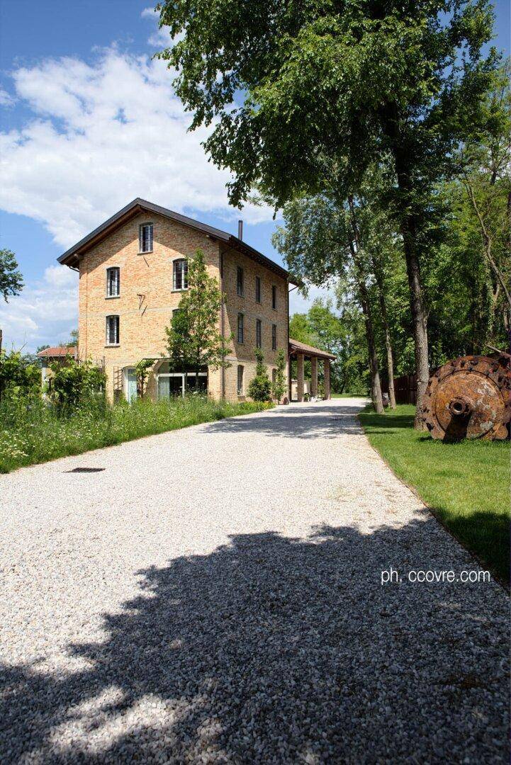 Das Ziegelsteinhaus mit langem Kiesweg, umgeben von Bäumen und einem dekorativen historischen Rad.