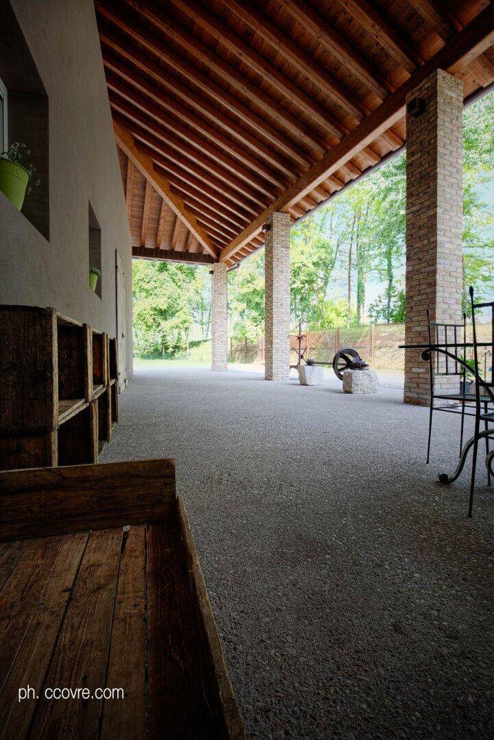 Überdachter Außenbereich mit Holzbalken und Ziegelpfeilern, der einen Blick ins Grüne bietet.