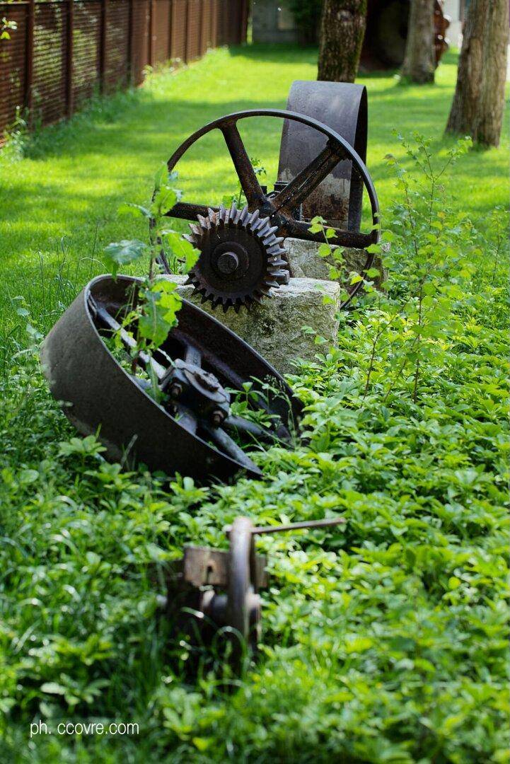 Alte rostige Industrie-Räder und Zahnräder als Dekoration in einem üppig grünen Gartenbereich.