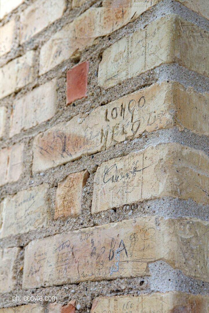 Nahaufnahme einer alten Backsteinwand mit eingravierten Inschriften und Spuren der Zeit.