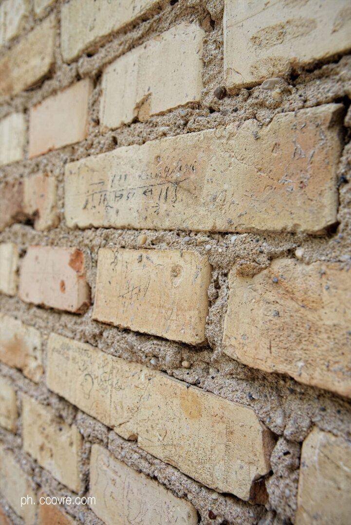 Nahaufnahme einer alten Backsteinwand mit eingravierten Inschriften und Spuren der Zeit.