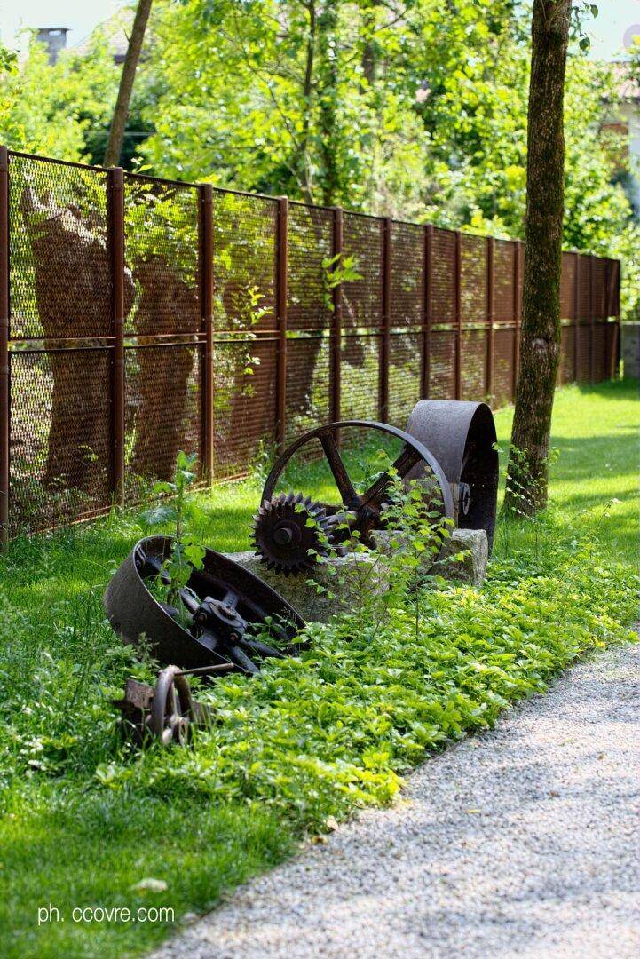 Alte rostige Industrie-Räder und Zahnräder als Dekoration in einem üppig grünen Gartenbereich.