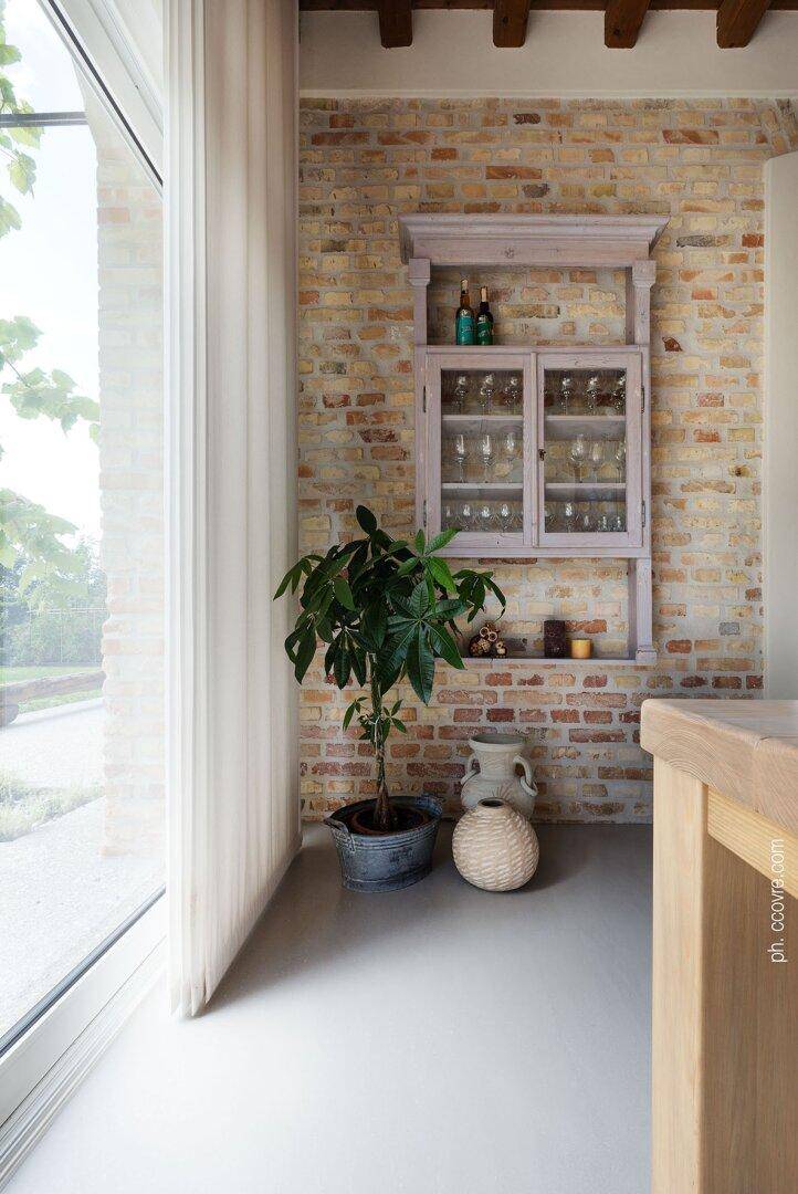 Detailansicht einer Backsteinwand mit Hängeschrank, Zimmerpflanze und großem Fenster.