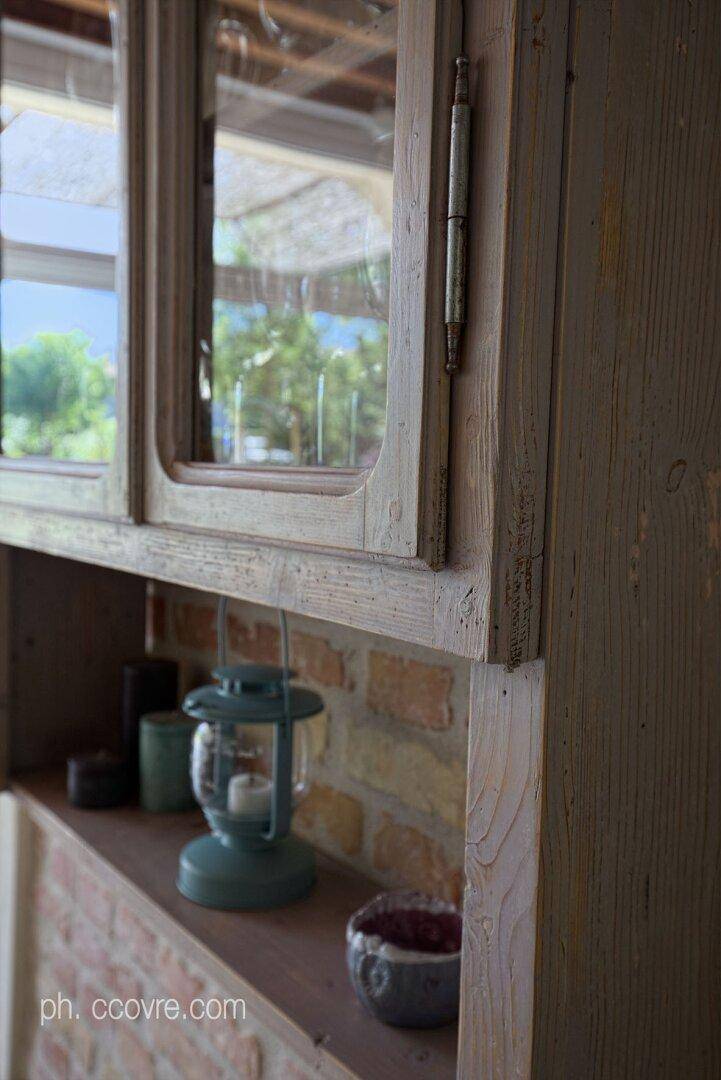 Nahaufnahme eines Holzschranks mit Glasfront und dekorativen Elementen auf einem gemauerten Regal.