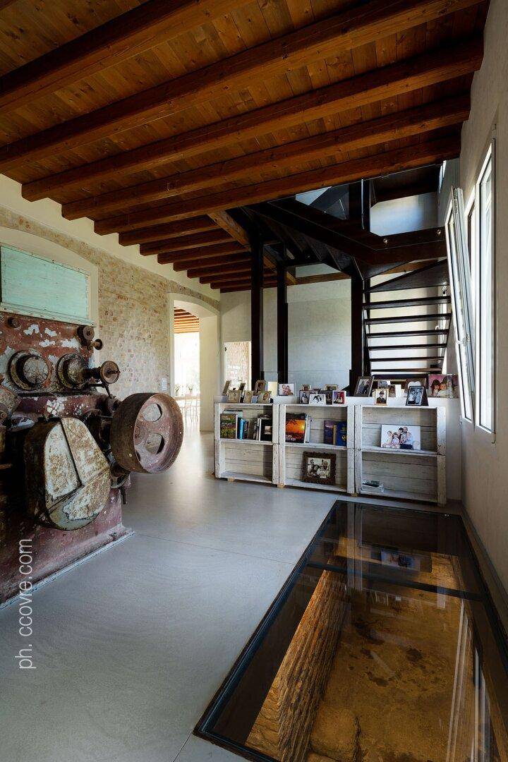 Offener Bereich mit Holzbalkendecke, moderner Treppe und einem dekorativen historischen Industrieobjekt.