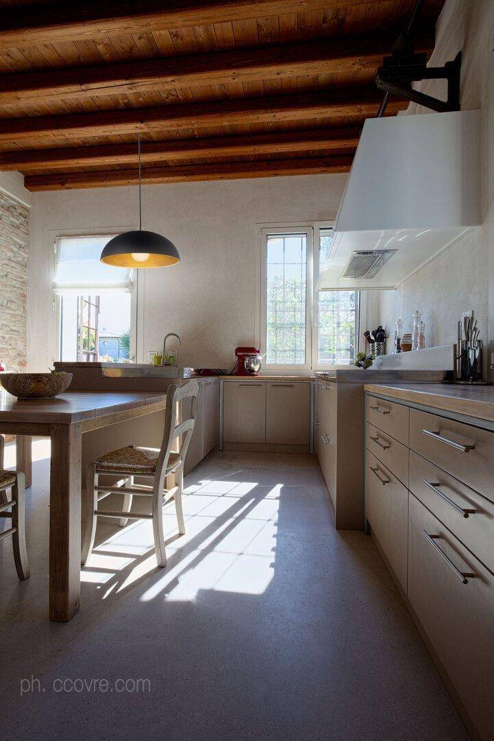 Helle Küche mit Holzbalkendecke, modernem Esstisch und großen Fenstern für viel Tageslicht.