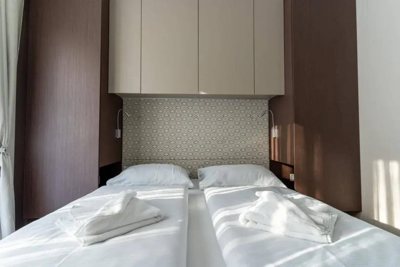 Helles Schlafzimmer mit zwei Einzelbetten, integrierten Schränken und dekorativem Kopfteil.