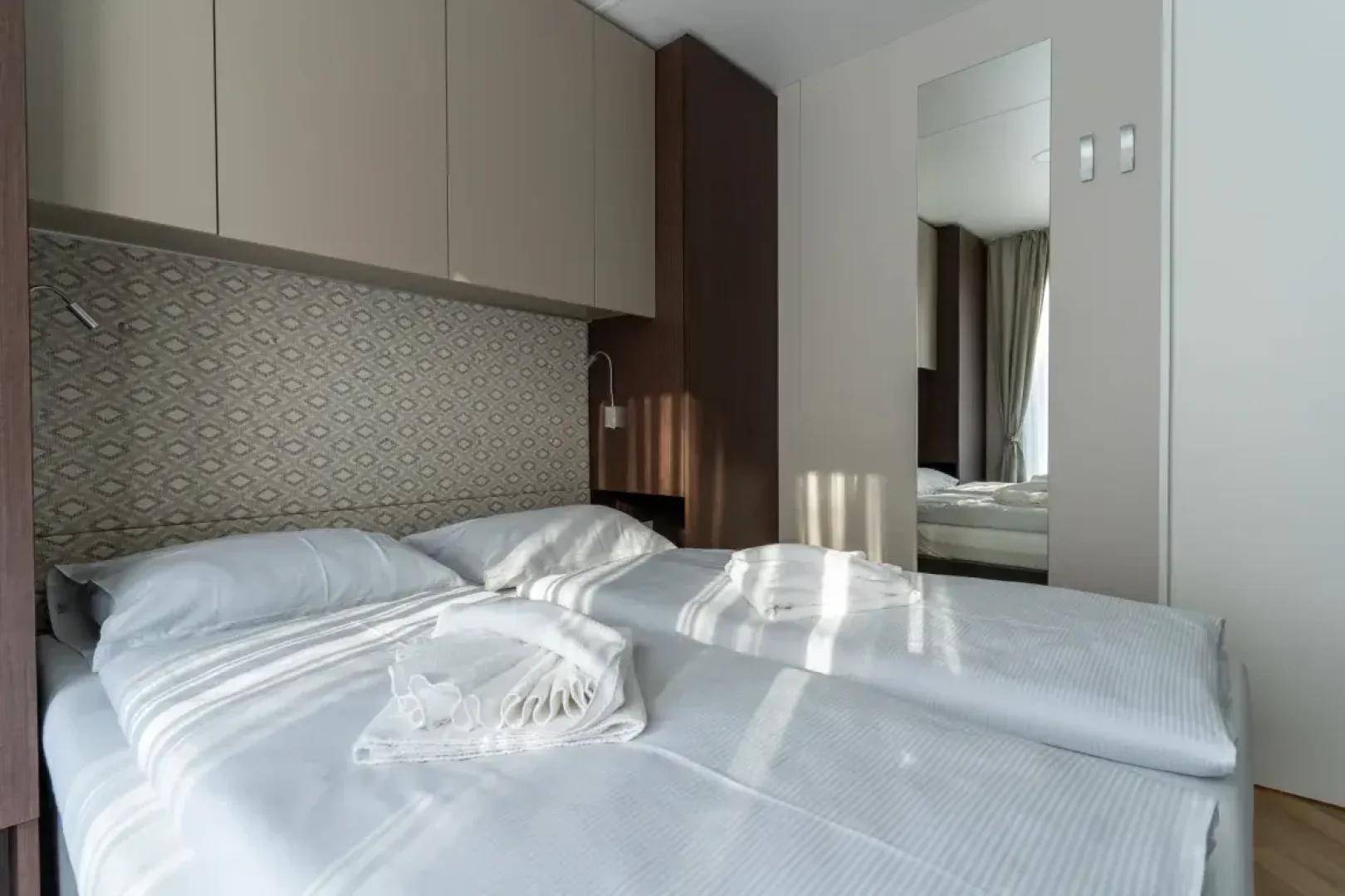 Freundliches Schlafzimmer mit zwei Einzelbetten, praktischen Einbauschränken und einem großen Spiegel.