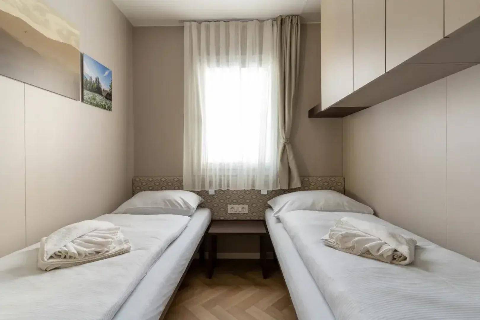 Helles Schlafzimmer mit zwei Einzelbetten, kleinem Nachttisch und integrierten Oberschränken.