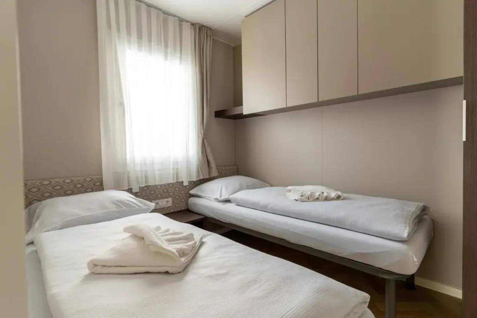 Gemütliches Schlafzimmer mit zwei Einzelbetten, einem Fenster und praktischen Hängeschränken.
