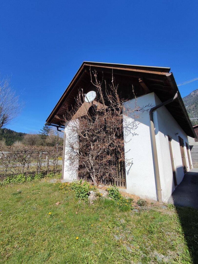 Kleines Nebengebäude mit Holztür und Satteldach neben dem Haupthaus in ländlicher Umgebung.