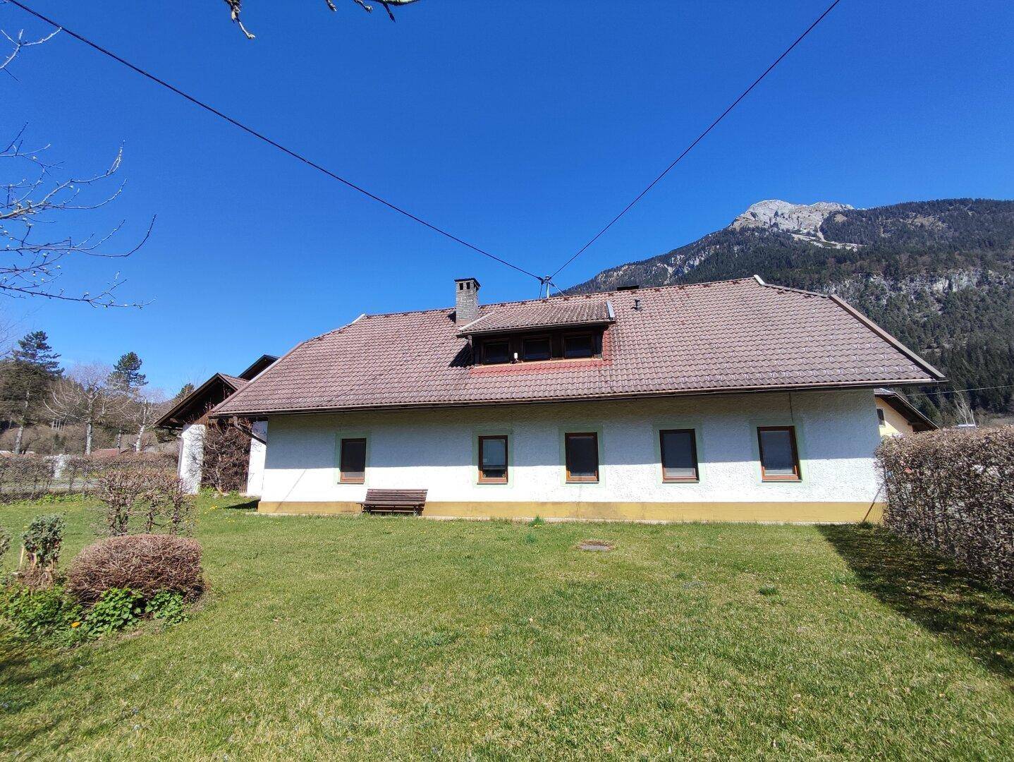 Rückansicht des Hauses mit Garten und Blick auf die umliegende Berglandschaft an einem sonnigen Tag.
