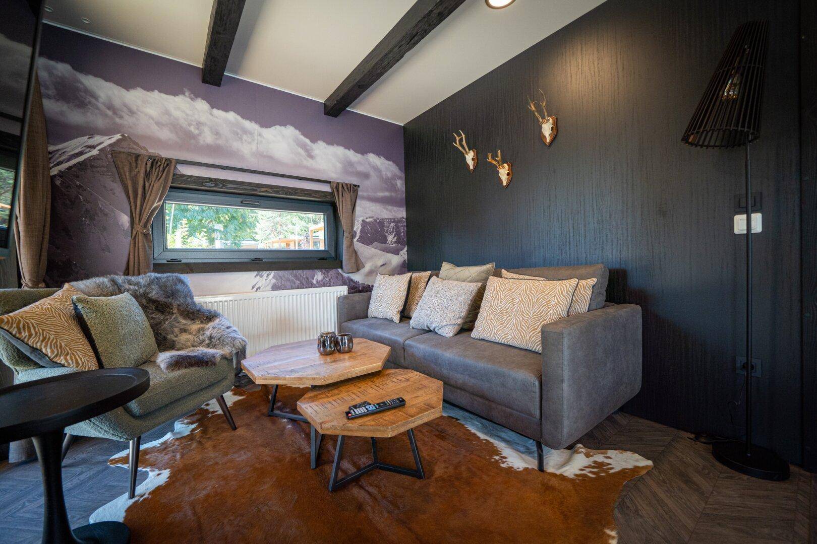 Helles Wohnzimmer mit bequemen Möbeln, Kuhfellteppich und Berglandschaft-Tapete.