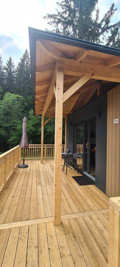 Geräumige Holzterrasse mit Sitzgelegenheiten und Zugang zum Ferienhaus, umgeben von Bäumen.